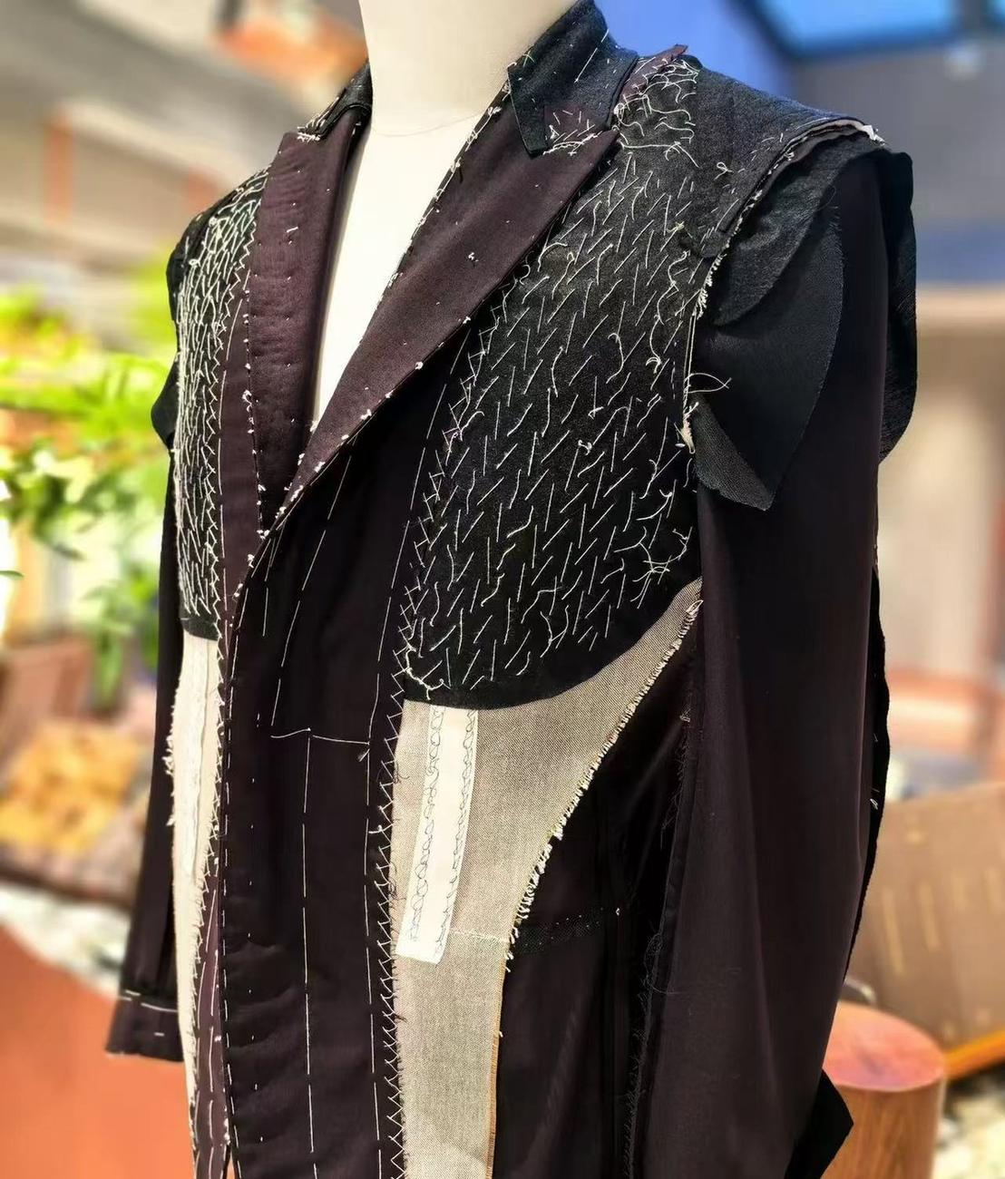 An unfinished jacket on a dress form with the lapel and chest canvas pad-stitched by hand, rows of white basting thread visible.