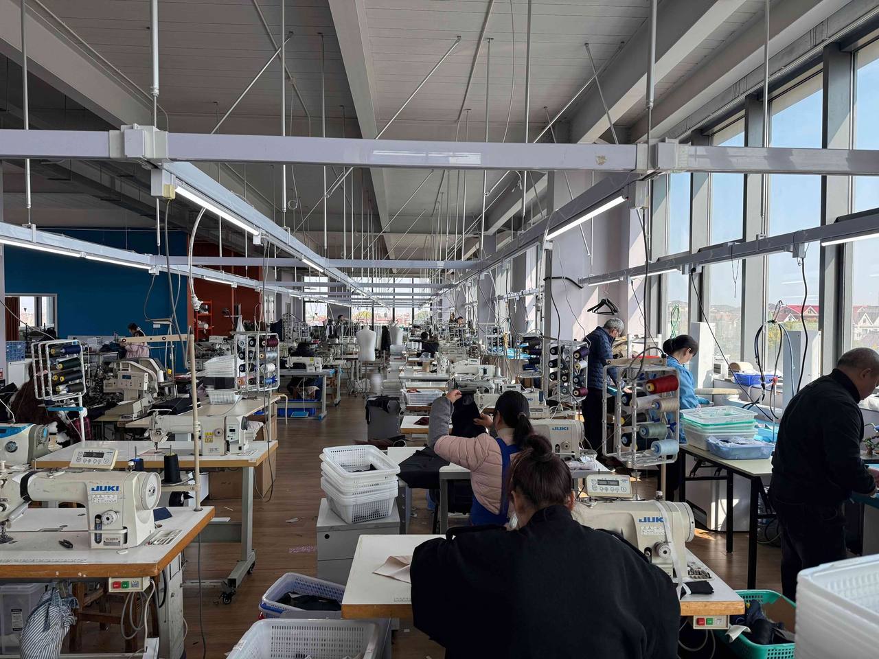 The sewing floor of our workshop in Shanghai, with rows of machines, pressing tables and tailors at work.